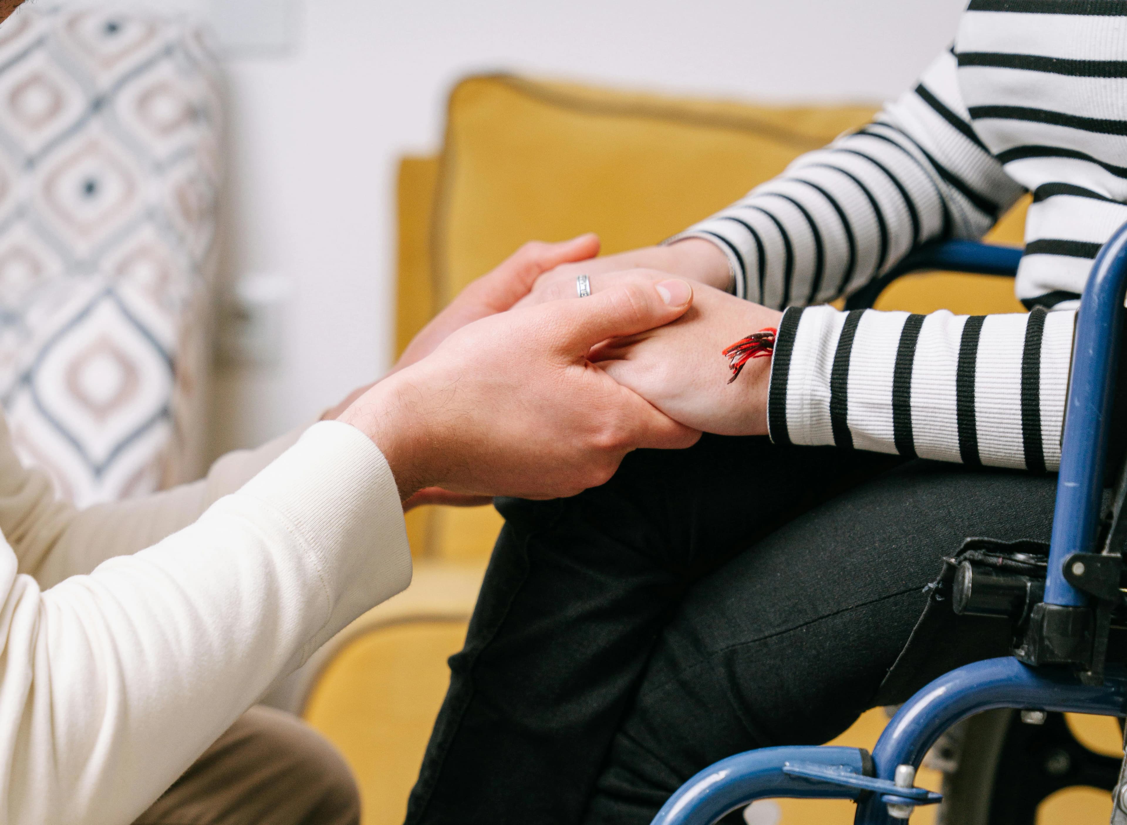 Girl in wheelchair holding hands with care giver
